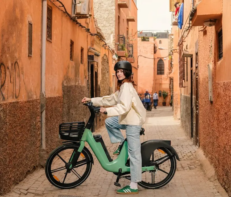 A young woman on an e-bike riding through a narrow ochre alley in the Medina
